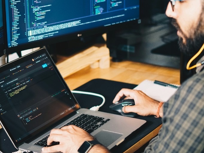Developer working at a laptop and external monitor with code on screen, representing infrastructure-as-code adoption.