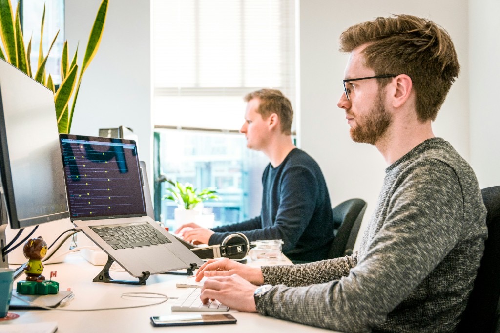 Two software engineers collaborating on infrastructure code at a bright modern office desk.